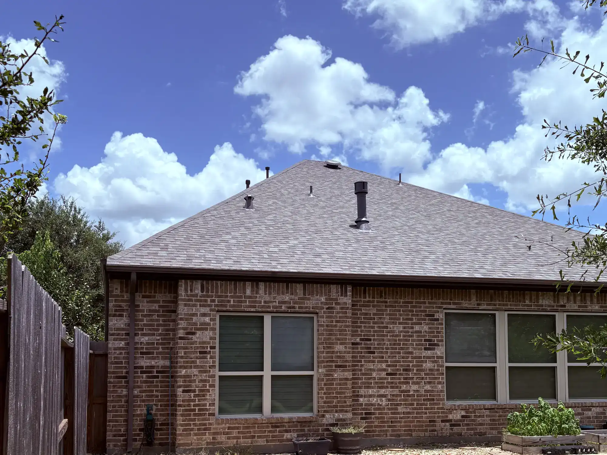Residential architectural-shingle roof under a bright Texas sky.